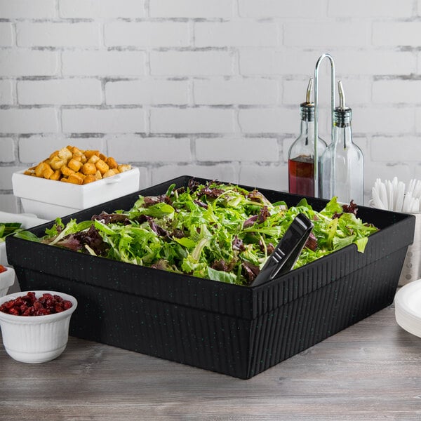 A salad in a Tablecraft black cast aluminum bowl with green speckles on a table.