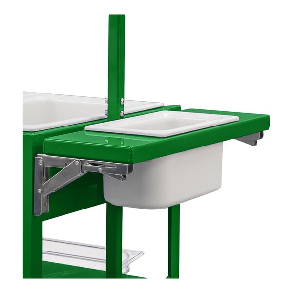 A partial view of a green metal cart with a foldable shelf holding a white rectangular pan and a white bin underneath.