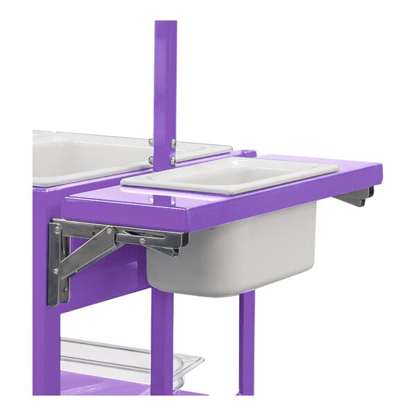 A partial view of a purple metal cart with a foldable shelf holding a white rectangular pan.