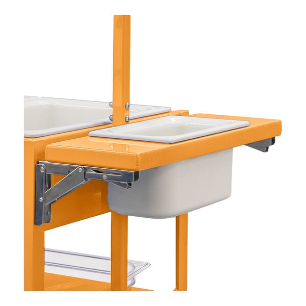A partial view of an orange metal cart with a foldable shelf holding a white rectangular pan.