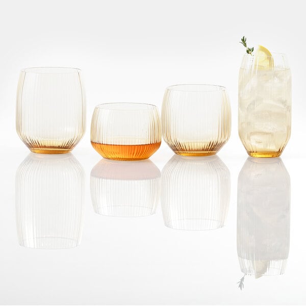 Four ribbed glasses are shown, three empty and one filled with a light beverage, ice, a lemon slice, and a sprig of herb.