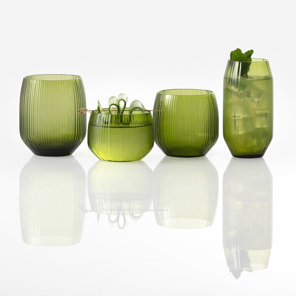 Four green, ribbed glass tumblers of varying shapes and sizes are arranged in a row, with one containing a drink garnished with mint and another holding a cocktail with a skewer.
