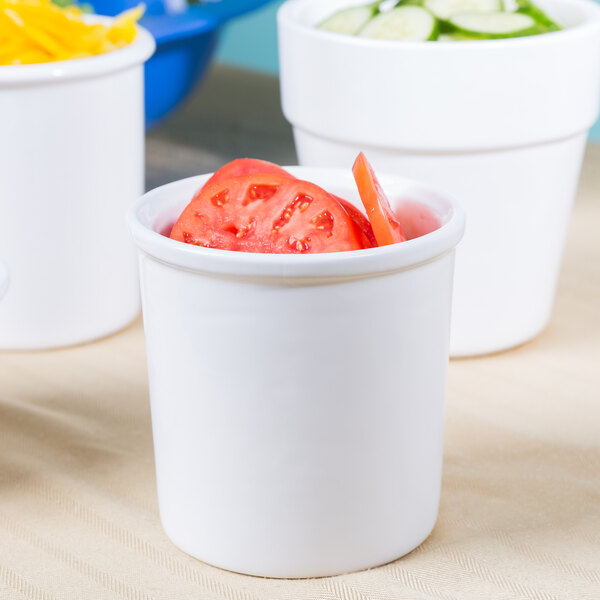 A close-up of a Tablecraft white cast aluminum condiment bowl filled with tomatoes and cucumbers.