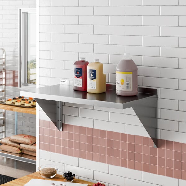 A heavy duty 18-inch by 36-inch stainless steel wall shelf mounted on a tiled wall, holding three condiment containers.