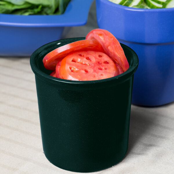 A hunter green bowl with white speckles full of sliced tomatoes on a counter.