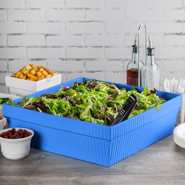 A cobalt blue square cast aluminum bowl with salad inside.