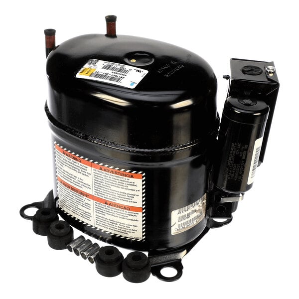 A black cylindrical mechanical component with attached electrical parts, warning labels, and several small rubber and metal fittings placed nearby.