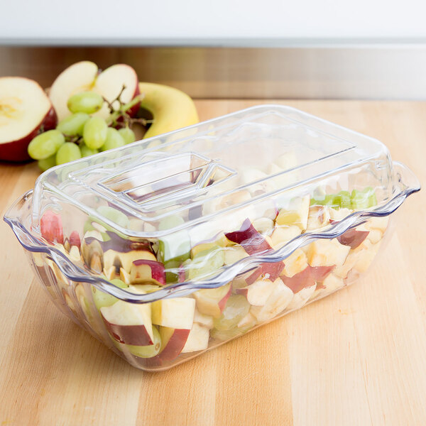 A clear rectangular plastic container with a lid, filled with chopped fruit pieces, sits on a wooden surface.