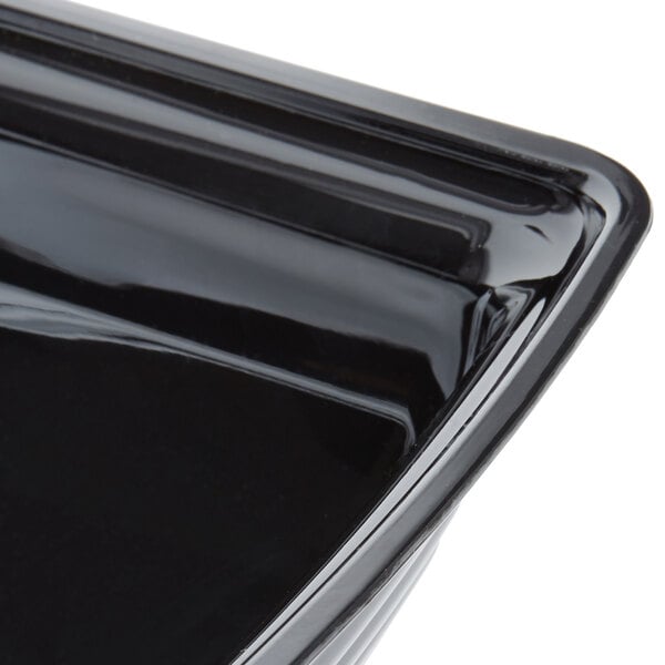 A close-up view of a glossy black rectangular bowl with ribbed edges.