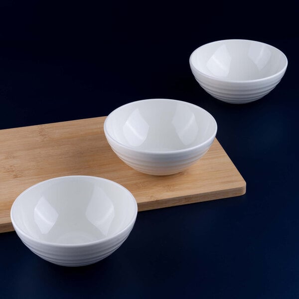 Three white porcelain bowls are arranged on and beside a wooden cutting board against a dark background.
