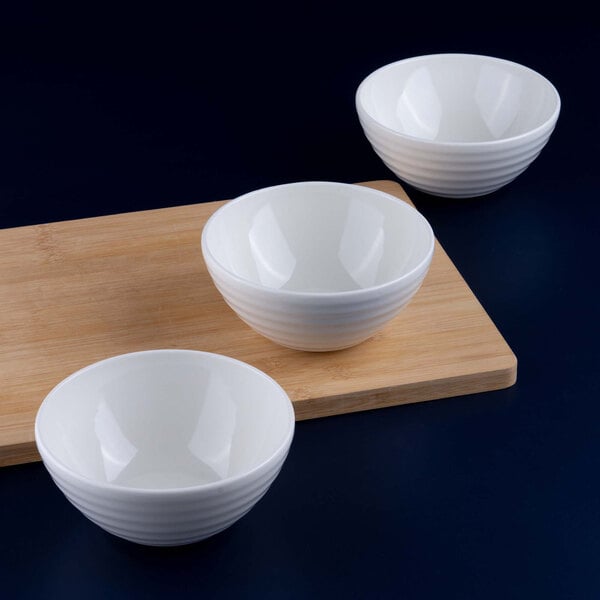Three white porcelain bowls are arranged near a wooden cutting board on a dark surface.