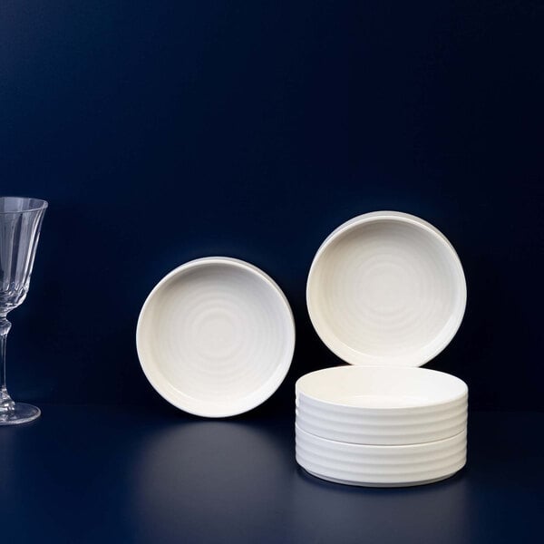 A set of round, ivory-colored porcelain bowls is displayed against a dark background, with two bowls standing upright and four stacked horizontally.