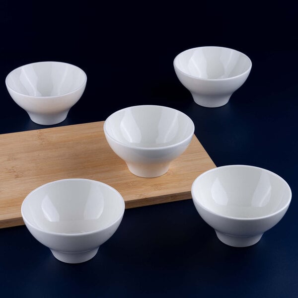 Five white porcelain bowls are arranged around a wooden board on a dark surface.