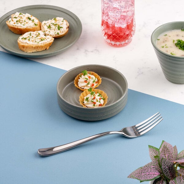 A small round green bowl containing two mini tartlets, placed on a blue and white surface with other food items and a fork nearby.