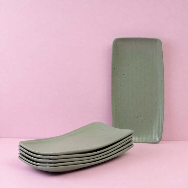 A stack of six rectangular green plates with one plate standing upright against a pink background.