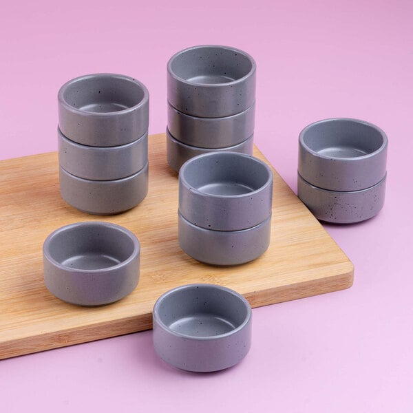 Several small, round, gray bowls are arranged on a wooden board and a pink surface.