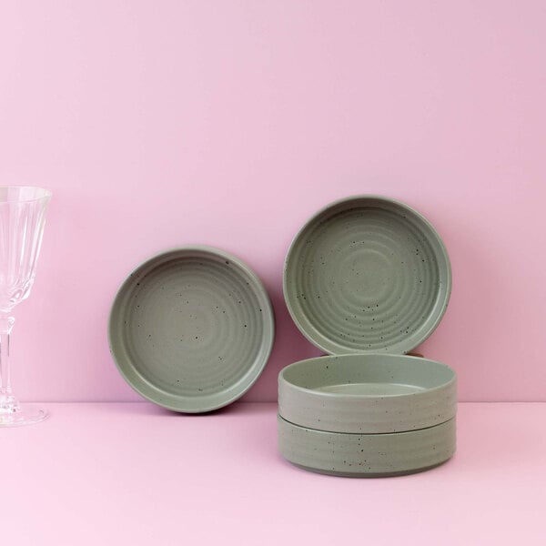 Four round, green bowls with a speckled pattern are displayed against a pink background, with two bowls stacked and two standing upright.