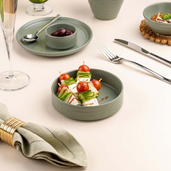 A round green bowl filled with skewered appetizers, placed on a table set with plates, cutlery, a napkin, and a glass.
