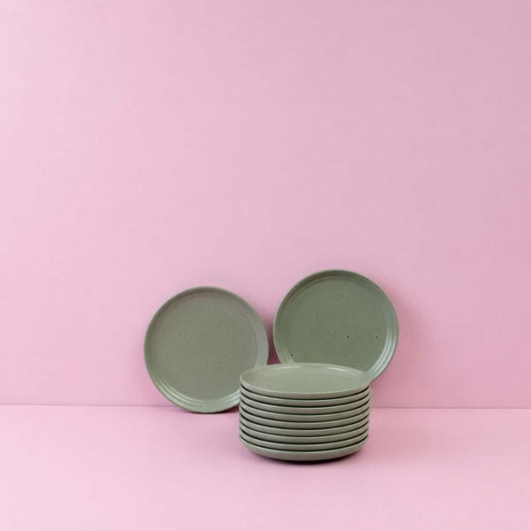 A stack of light green round plates with two additional plates standing upright behind them, set against a pink background.