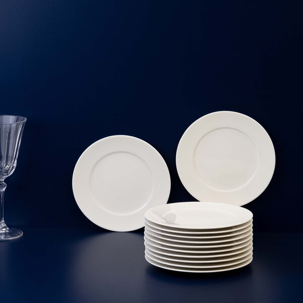A stack of plain white round plates is displayed in front of two upright plates, with a clear wine glass to the left, all set against a dark background.