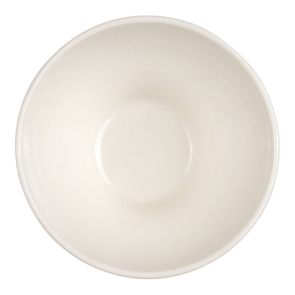 A small green ceramic bowl filled with a saucy dish, garnished with herbs, placed on a light-colored table with cutlery, a napkin, and other tableware nearby.