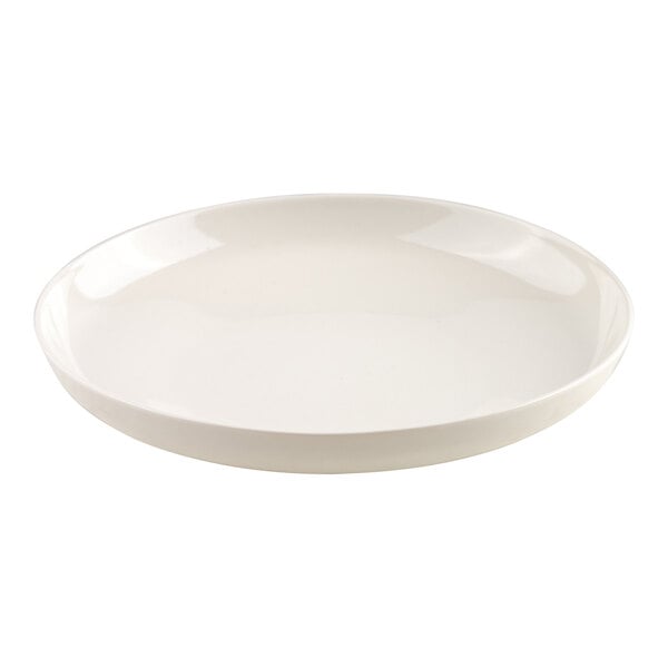 A stack of twelve plain, round, ivory-colored plates is shown with one plate standing upright behind the stack, and a clear wine glass is partially visible on the left side.