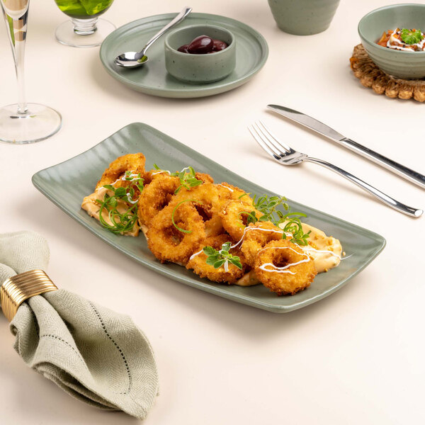 A rectangular green platter with a serving of breaded and fried rings garnished with herbs and sauce, placed on a set dining table.