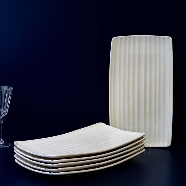 A set of six rectangular, ivory-colored platters with a ribbed texture, stacked together with one platter standing upright in the background.