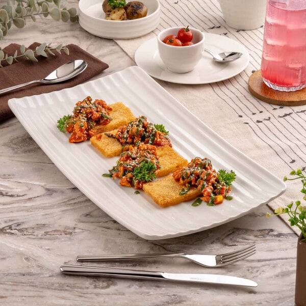 A large rectangular ivory platter with a wavy textured surface, holding four pieces of golden fried food topped with a colorful vegetable mixture and garnished with fresh herbs.