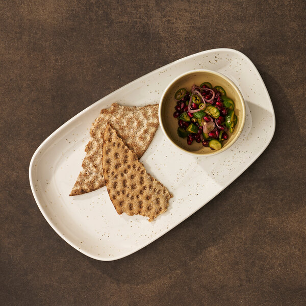 A white oval tray with two pieces of crispbread and a small bowl of colorful salad.