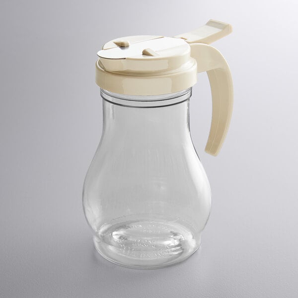 A clear glass syrup server with a cream-colored plastic lid and handle.