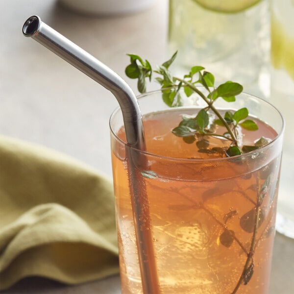 A glass of iced beverage with a stainless steel bent straw and a sprig of fresh herbs as garnish.