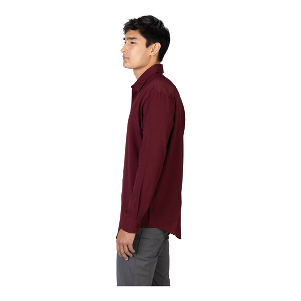 A man is standing in profile wearing a long-sleeve burgundy shirt and gray pants against a white background.