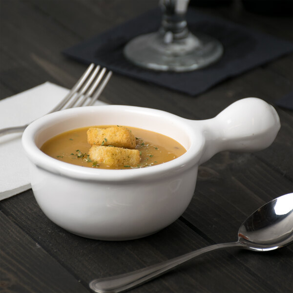 A white Tablecraft cast aluminum bowl of soup with a spoon.