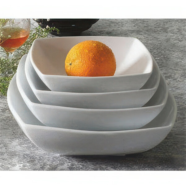 A stack of square white porcelain bowls with an orange in one of them.