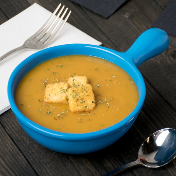 A Tablecraft sky blue cast aluminum soup bowl with a spoon next to it.