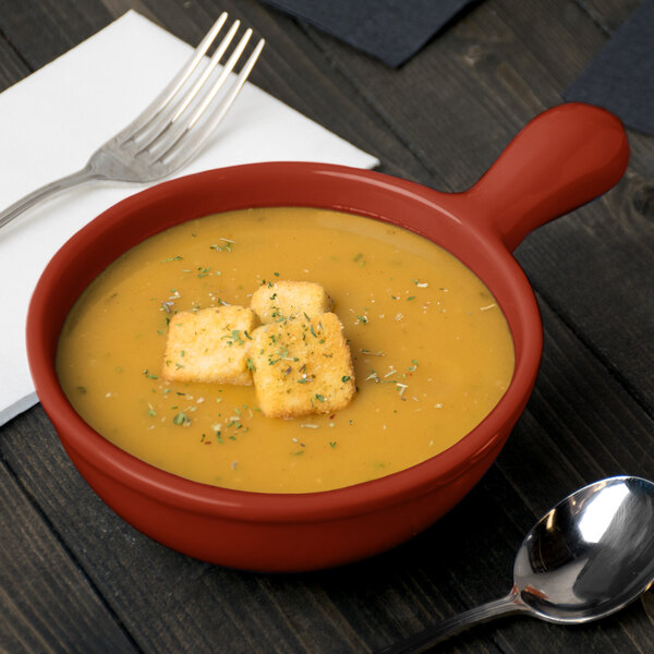 A Tablecraft copper cast aluminum soup bowl with croutons on top next to a spoon and fork.
