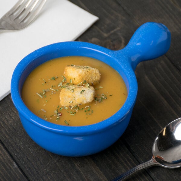 A blue Tablecraft cast aluminum bowl of soup with croutons and a spoon.