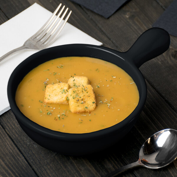 A Tablecraft black cast aluminum soup bowl with croutons on top served with a spoon and fork.