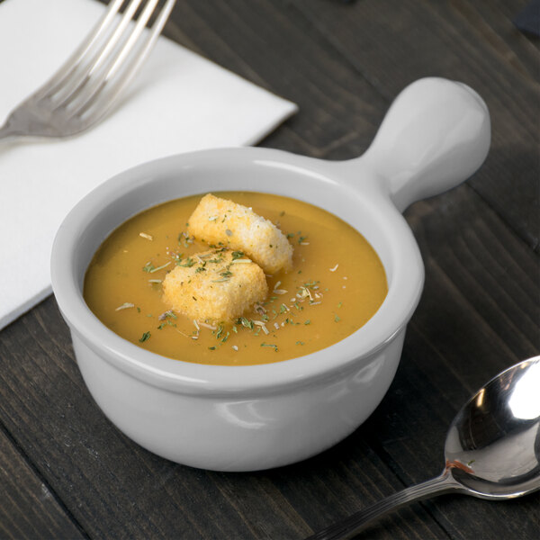 A Tablecraft natural cast aluminum soup bowl with a spoon next to it.