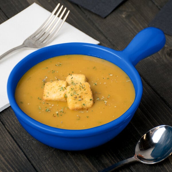 A cobalt blue cast aluminum bowl of soup with a spoon and a fork.