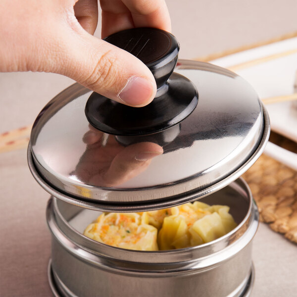 A hand holding a Town Stainless Steel Dim Sum Steamer Cover over food in a container.