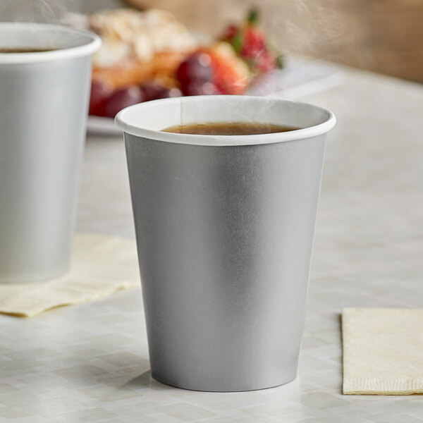 Two Creative Converting Shimmering Silver paper hot cups filled with a brown hot beverage on a table.