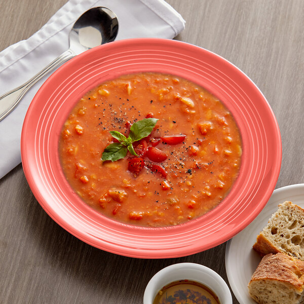 A Tuxton Cinnebar China bowl of soup with a spoon and a plate of bread.