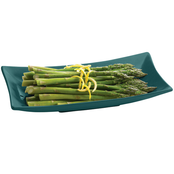 A Tablecraft hunter green cast aluminum flared rectangle platter with asparagus and lemon zest.