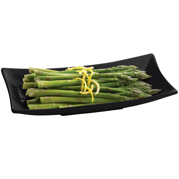 A black Tablecraft cast aluminum flared rectangular platter with asparagus and lemon slices.