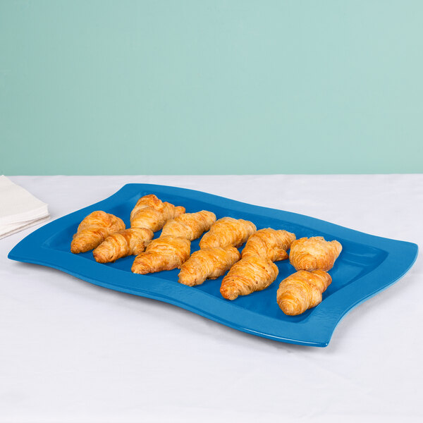 A Tablecraft sky blue rectangular metal platter with croissants on a table.