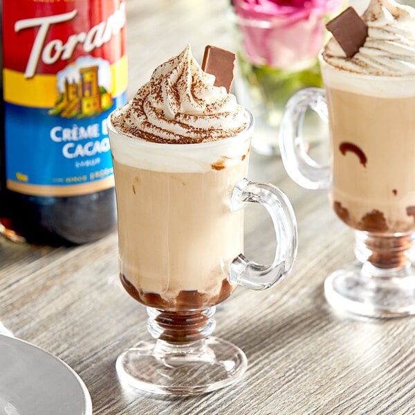 A glass cup of coffee with Torani Creme de Cacao syrup and whipped cream on a table.