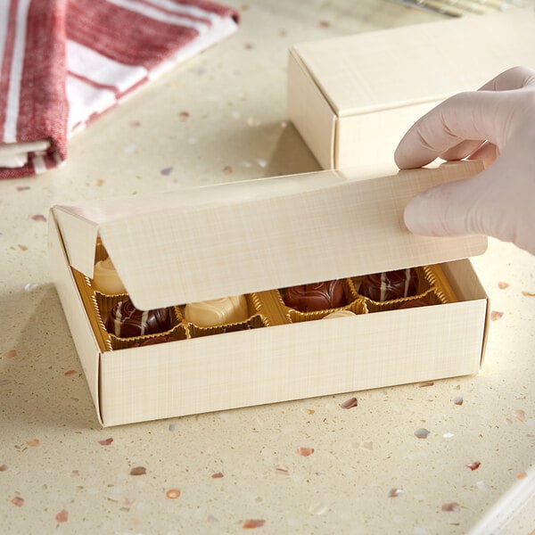 A gloved hand opens a gold linen candy box.