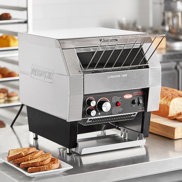 A Hatco TQ-400H conveyor toaster on a counter with a stack of bread.